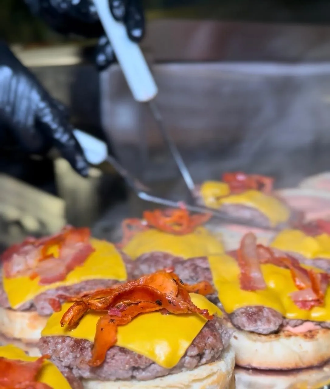La plancha en pleno servicio: medallones con cheddar y tocino, y una espátula.